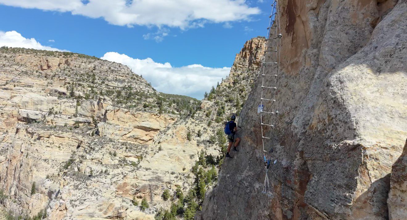 A climber on a hanging cable ladder above Ashley Gorge